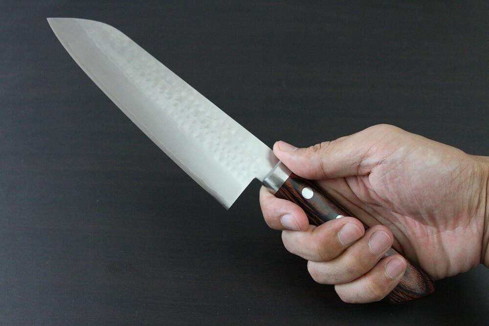 spsantoku_hamfin_maho_IMG_6240 Toshu Santoku multi-purpose Japanese chef's knife, hammered finish blade and mahogany handle, grabbed by a man's hand