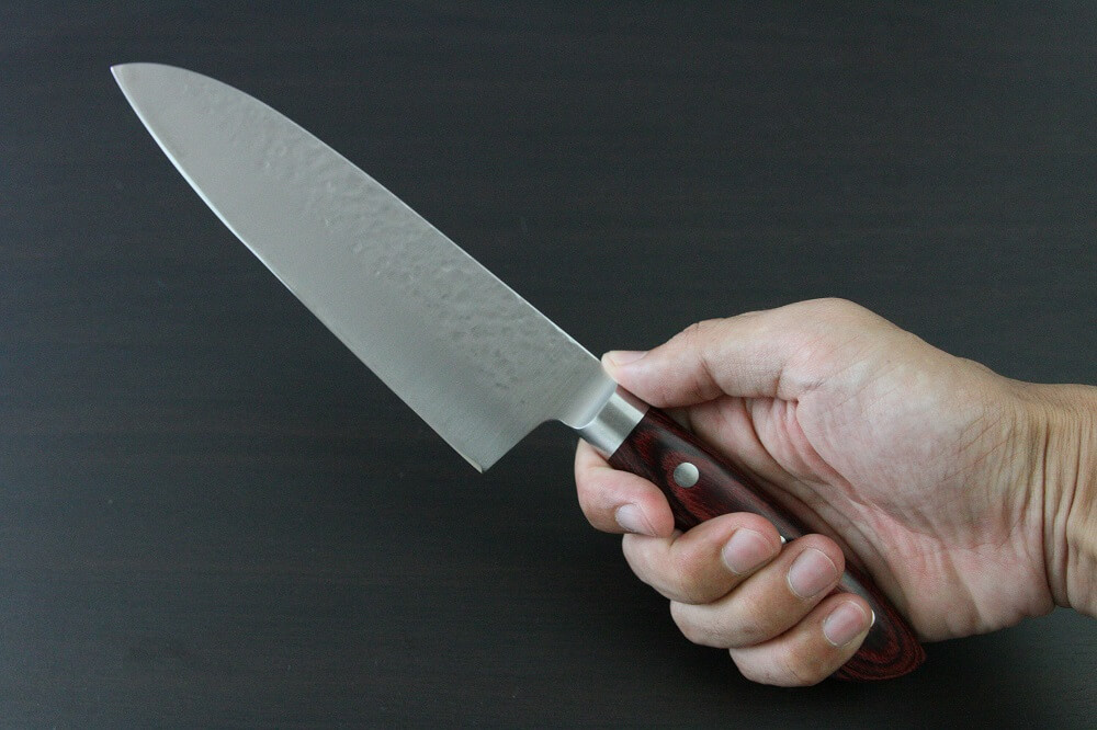 spsantoku_hamfin_red_IMG_6238 Toshu Santoku multi-purpose Japanese chef's knife, hammered finish blade and red handle, grabbed by a man's hand